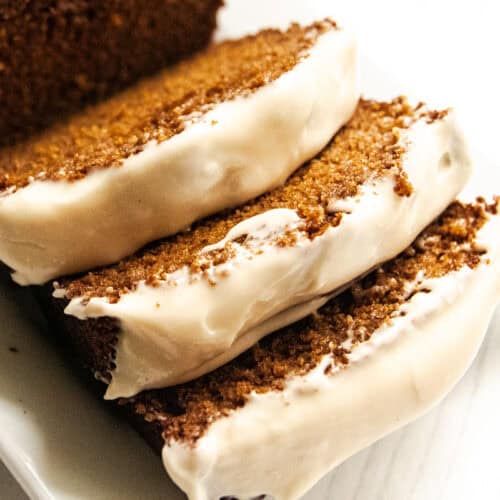 A sliced loaf of whole grain ginger bread with white frosting on top.
