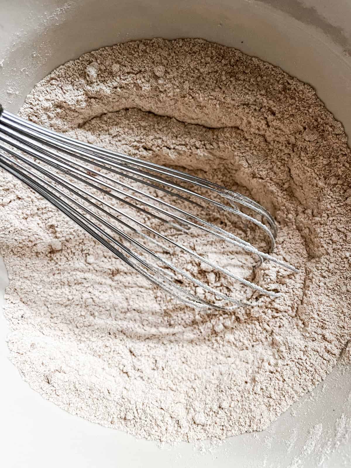 Stirring dry ingredients in a mixing bowl with a whisk.