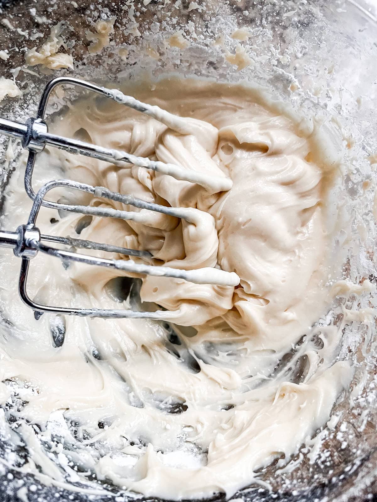 Homemade glaze in a glass bowl with hand mixer whisks.
