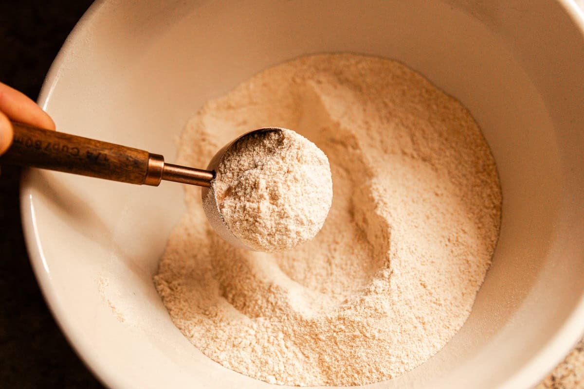 Scooping freshly milled whole grain flour out of a mixing bowl. 