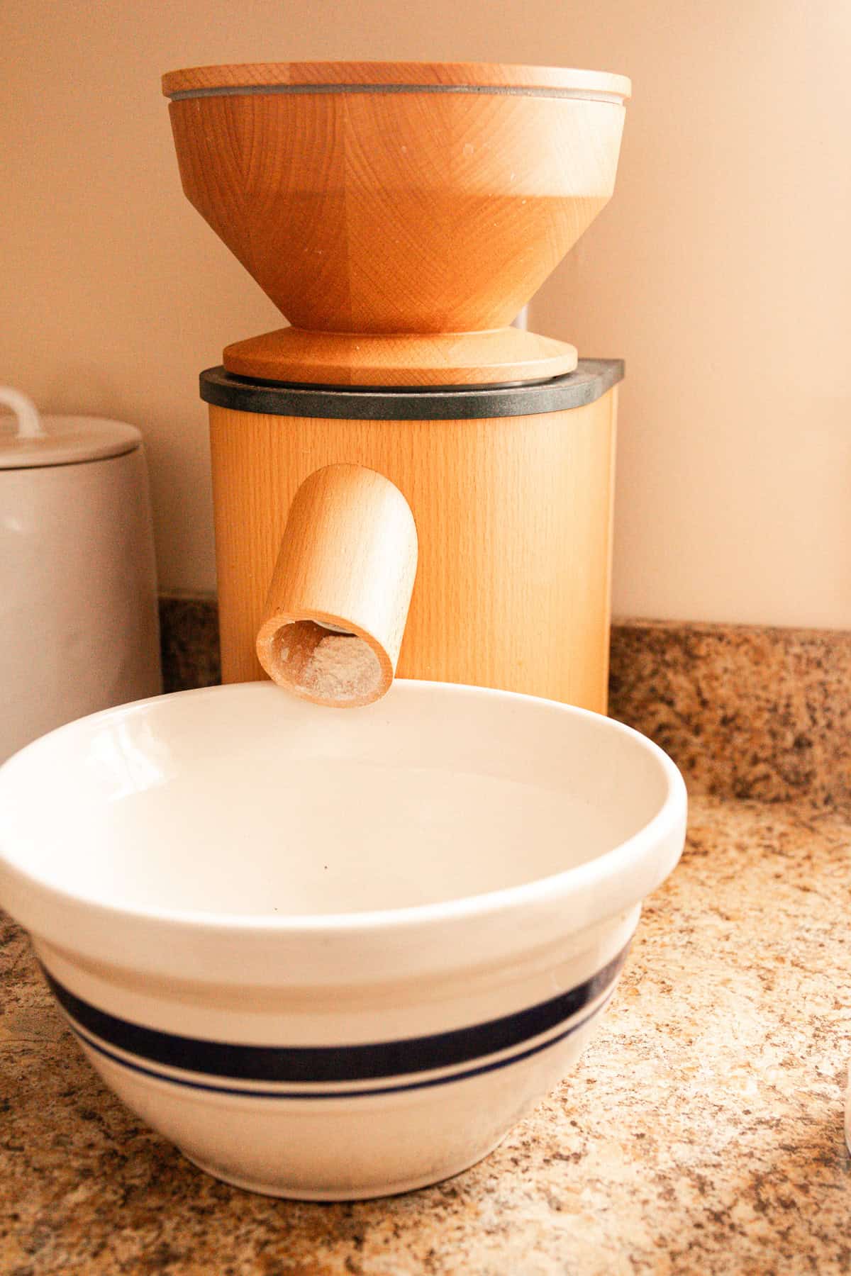A grain mill depositing freshly milled flour into a mixing bowl.