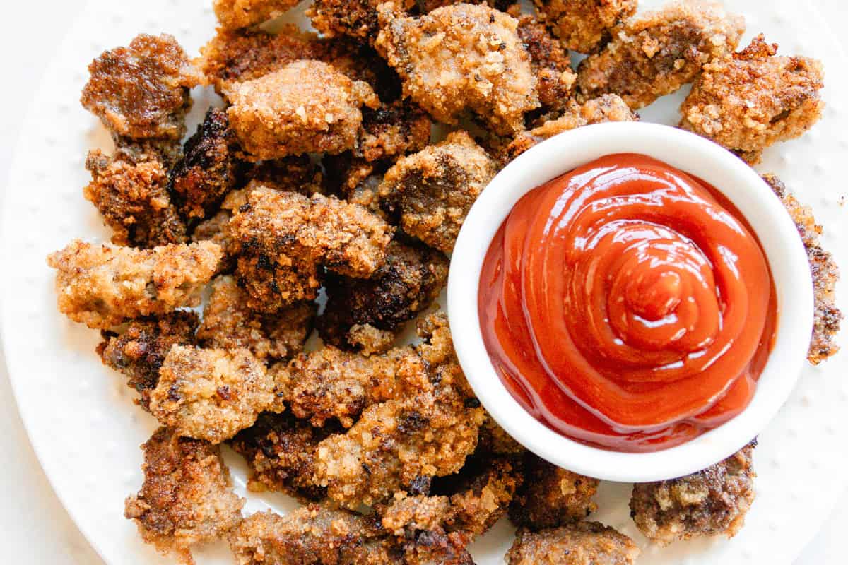 Venison nuggets on a white plate with a bowl of ketchup.