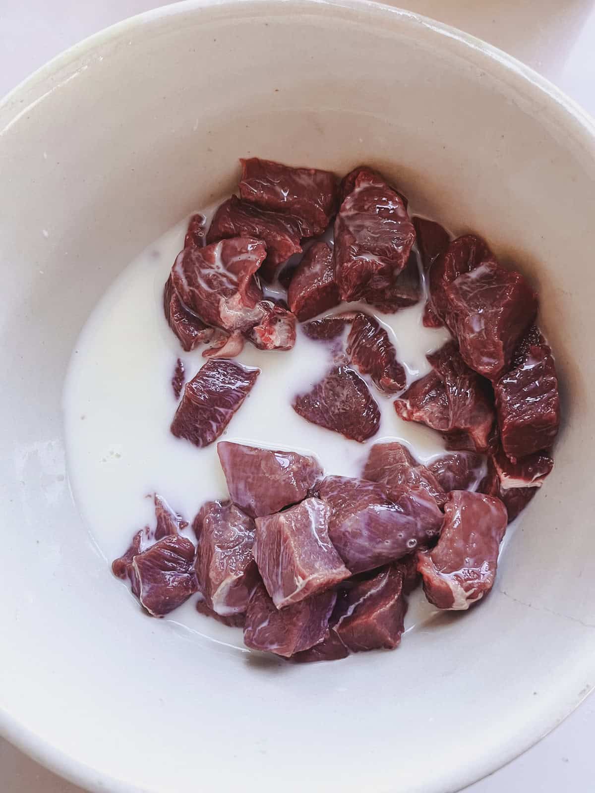 Cubed venison steak in a bowl with buttermilk.