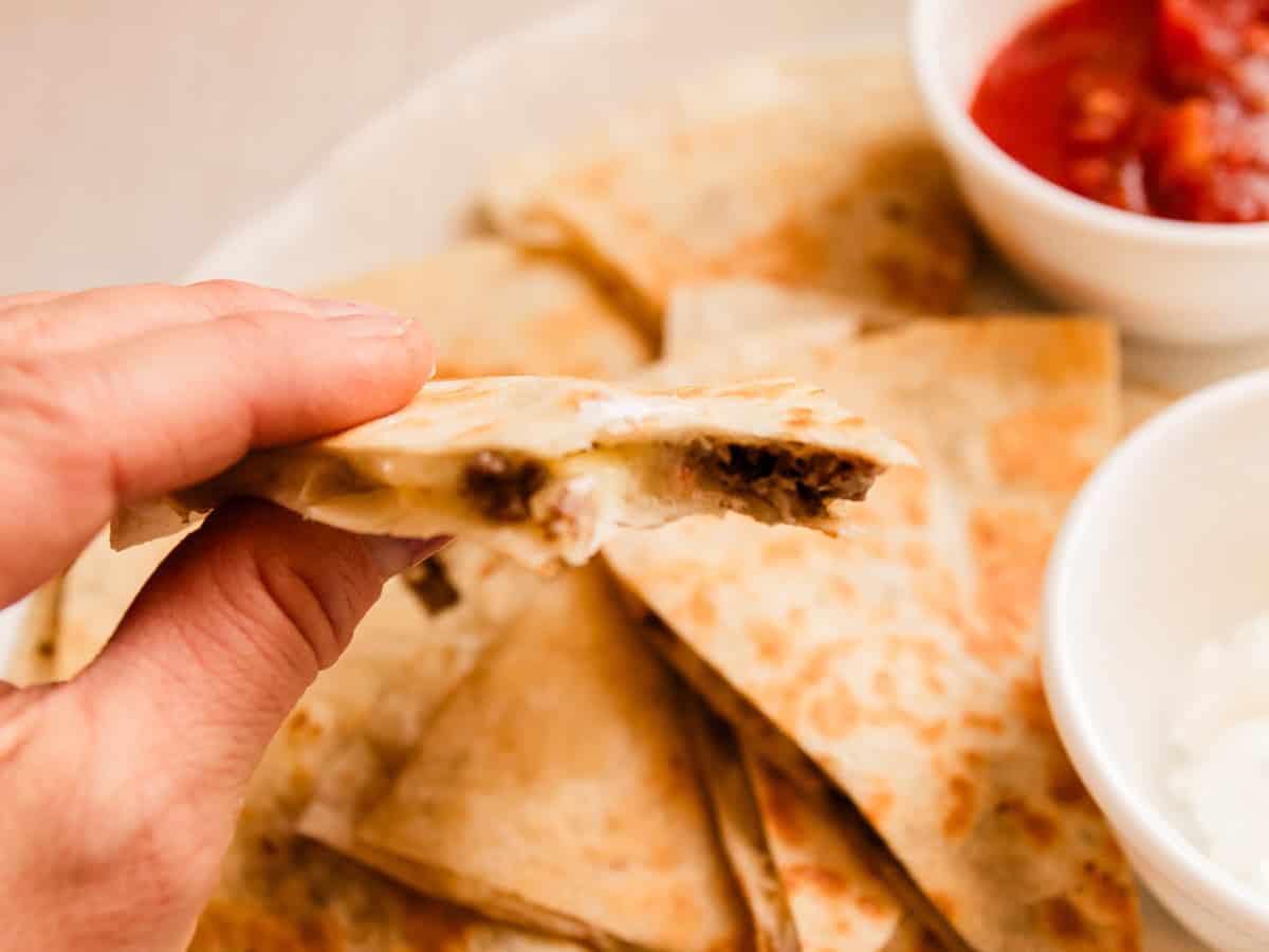 Holding up a slice of venison quesadilla over a plate of them.