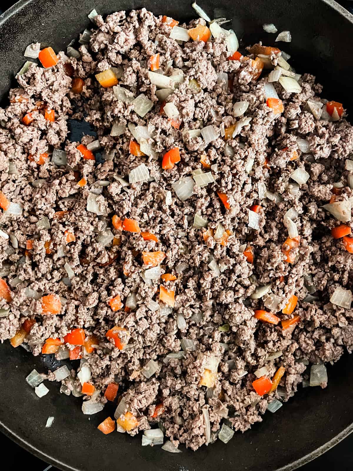 Browning ground venison with pepper and onions in a cast iron skillet.