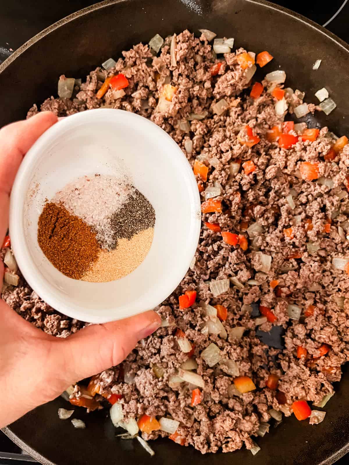 Pouring seasonings into the meat and veggie mixture.