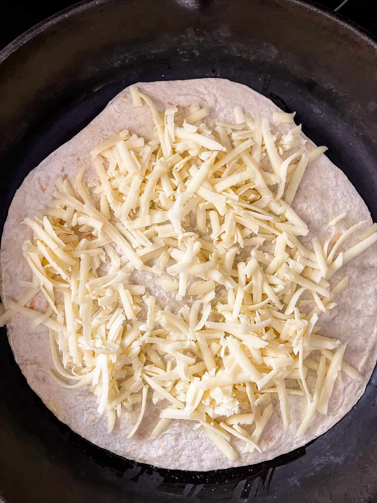 Spreading shredded cheese onto a flour tortilla.