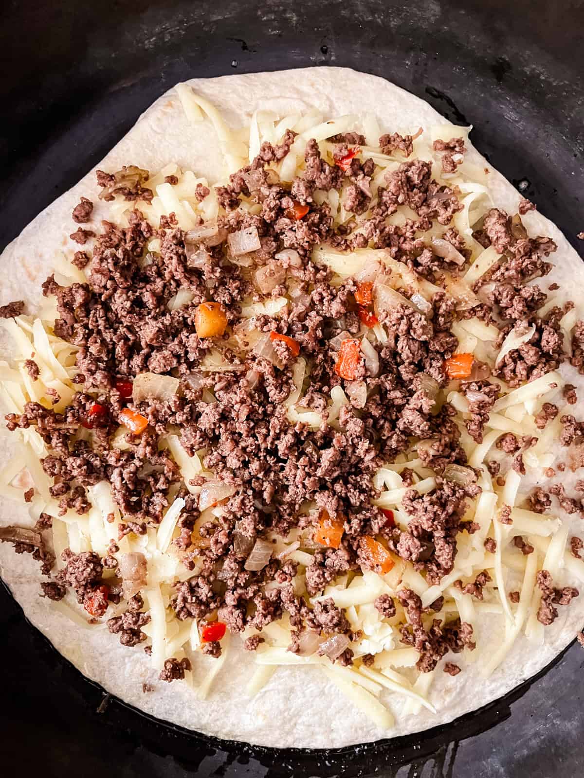 Spreading venison, peppers, and onions on a tortilla with cheese.