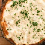 Venison shepherds pie in a cast iron skillet on a wooden tabletop.