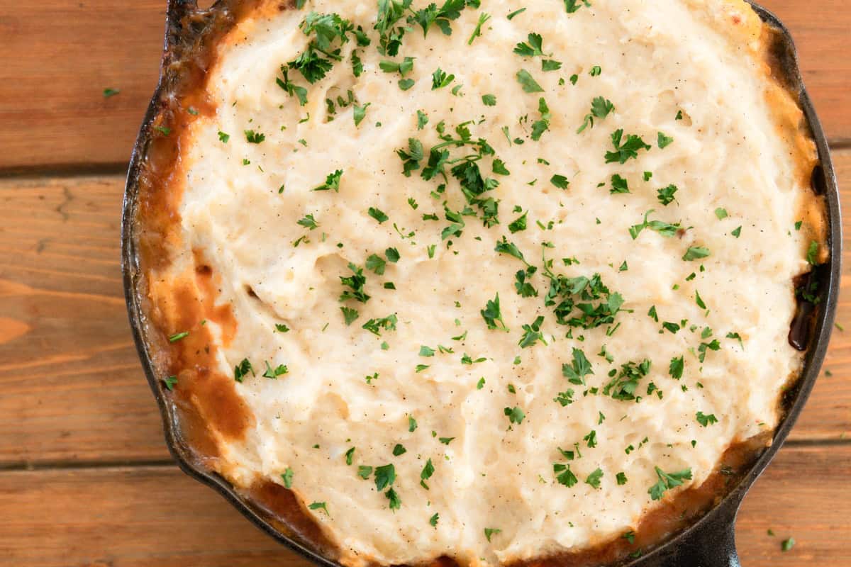 Venison shepherds pie in a cast iron skillet on a wooden tabletop.
