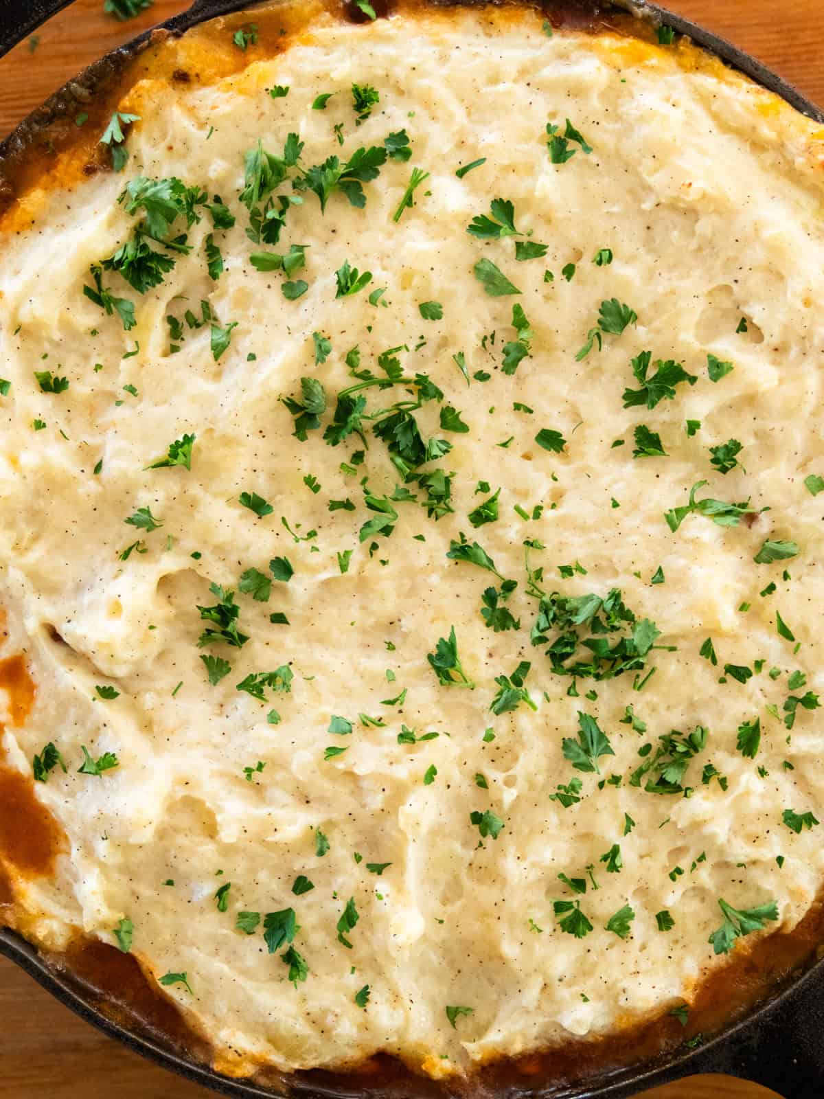 Venison shepherd's pie in a cast iron skillet with fresh parsley sprinkled on top.