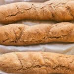 Three baguettes with freshly milled flour lined up on a baking sheet with parchment paper.