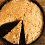 Looking down on a cast iron skillet of cornbread with freshly milled flour. It is sliced like a pizza with one slice missing.