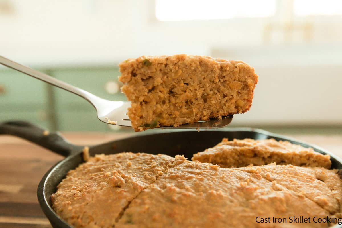 Lifting a slice of cornbread with freshly milled flour out of a cast iron skillet.