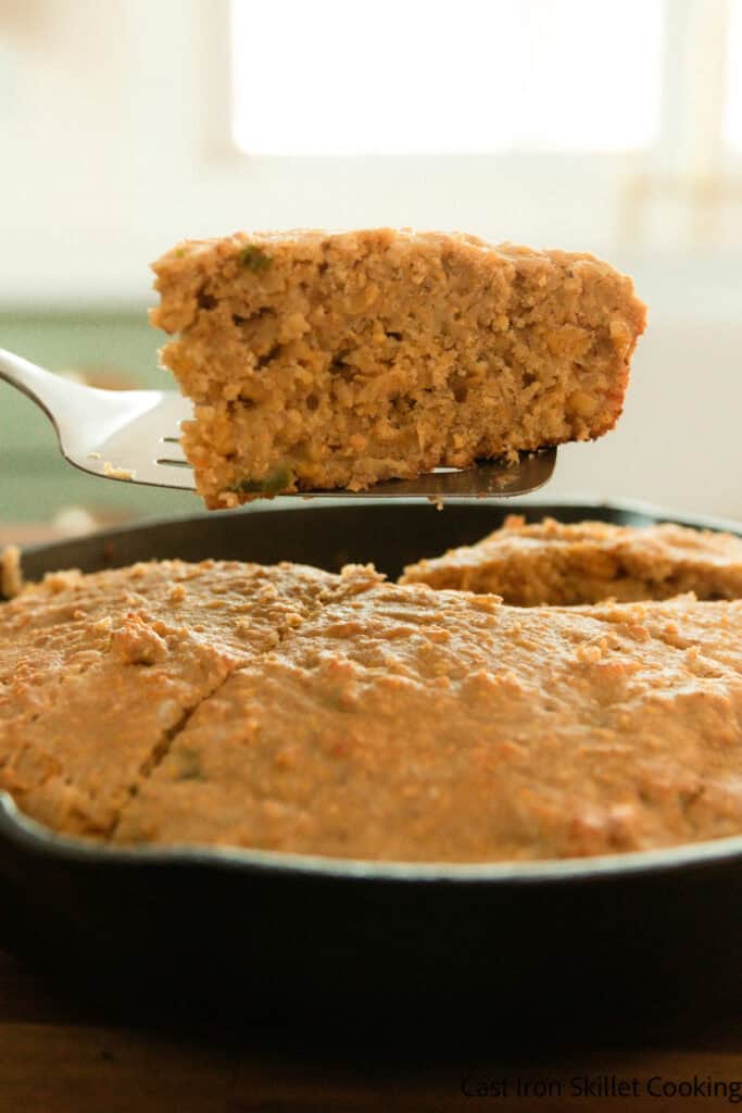 Lifting a slice of cornbread with freshly milled flour out of a cast iron skillet with a spatula.