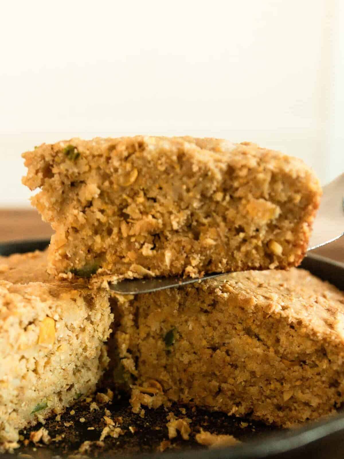 Lifting a slice of fresh milled cornbread out of a cast iron skillet with a spatula.