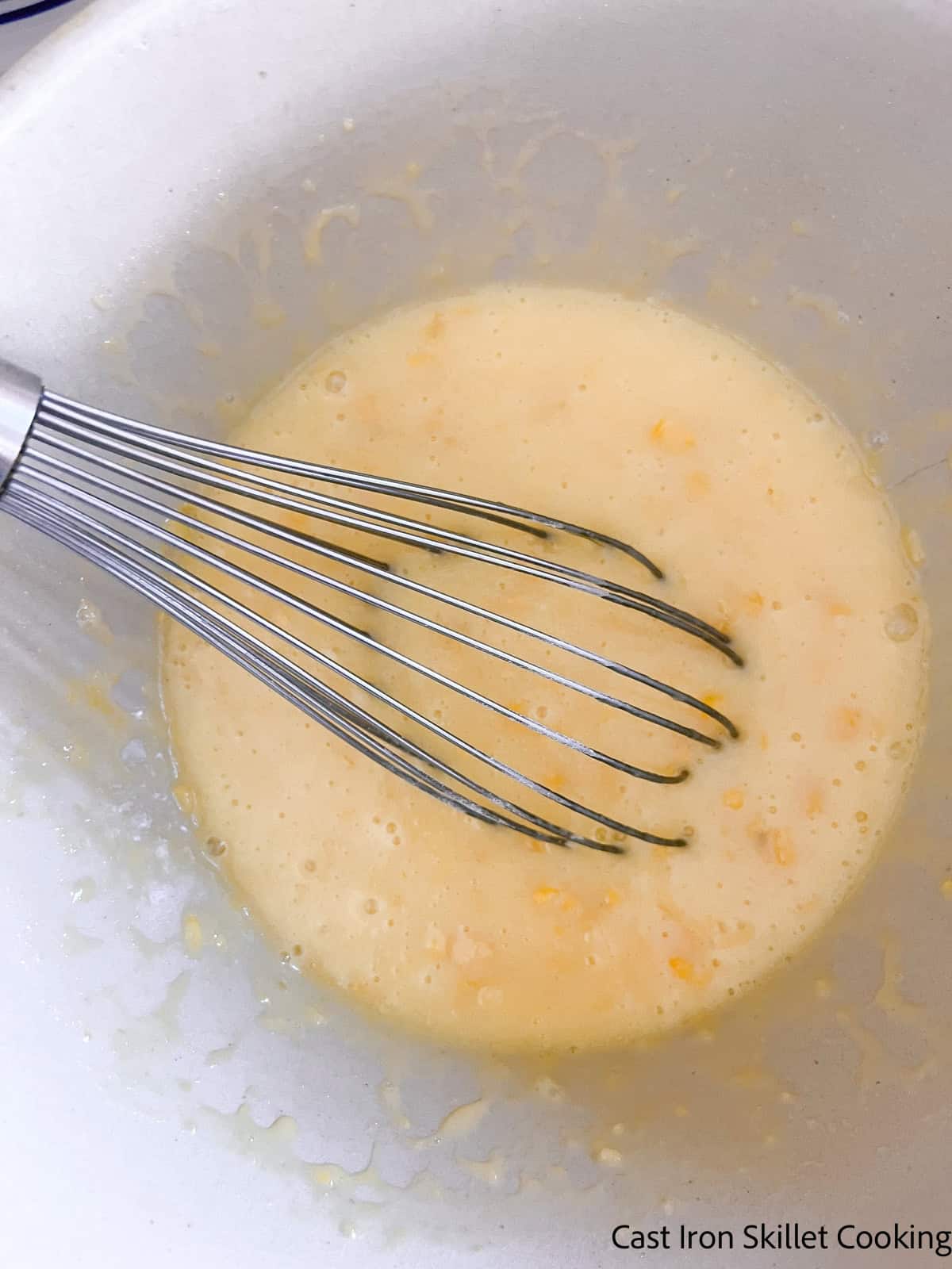 Mixing wet ingredients in a bowl with a whisk.