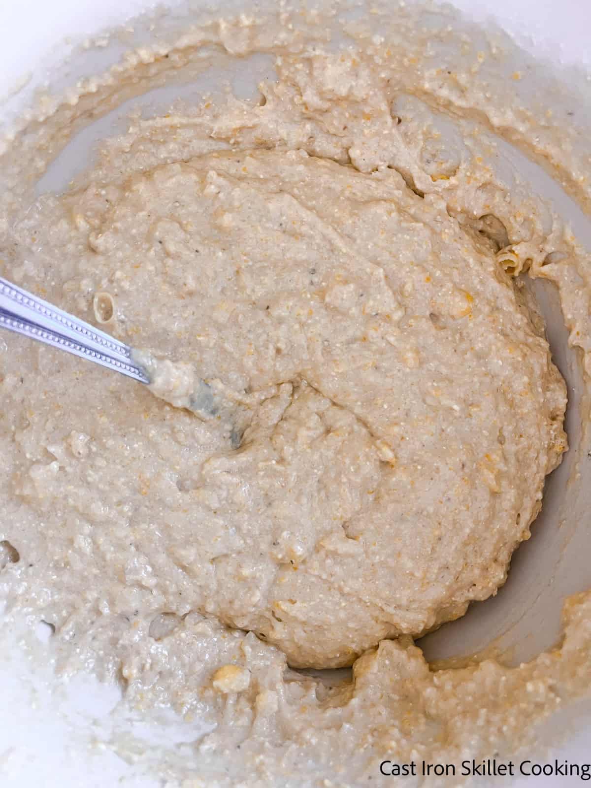Mixing cornbread with freshly milled flour batter in a bowl with a spoon.