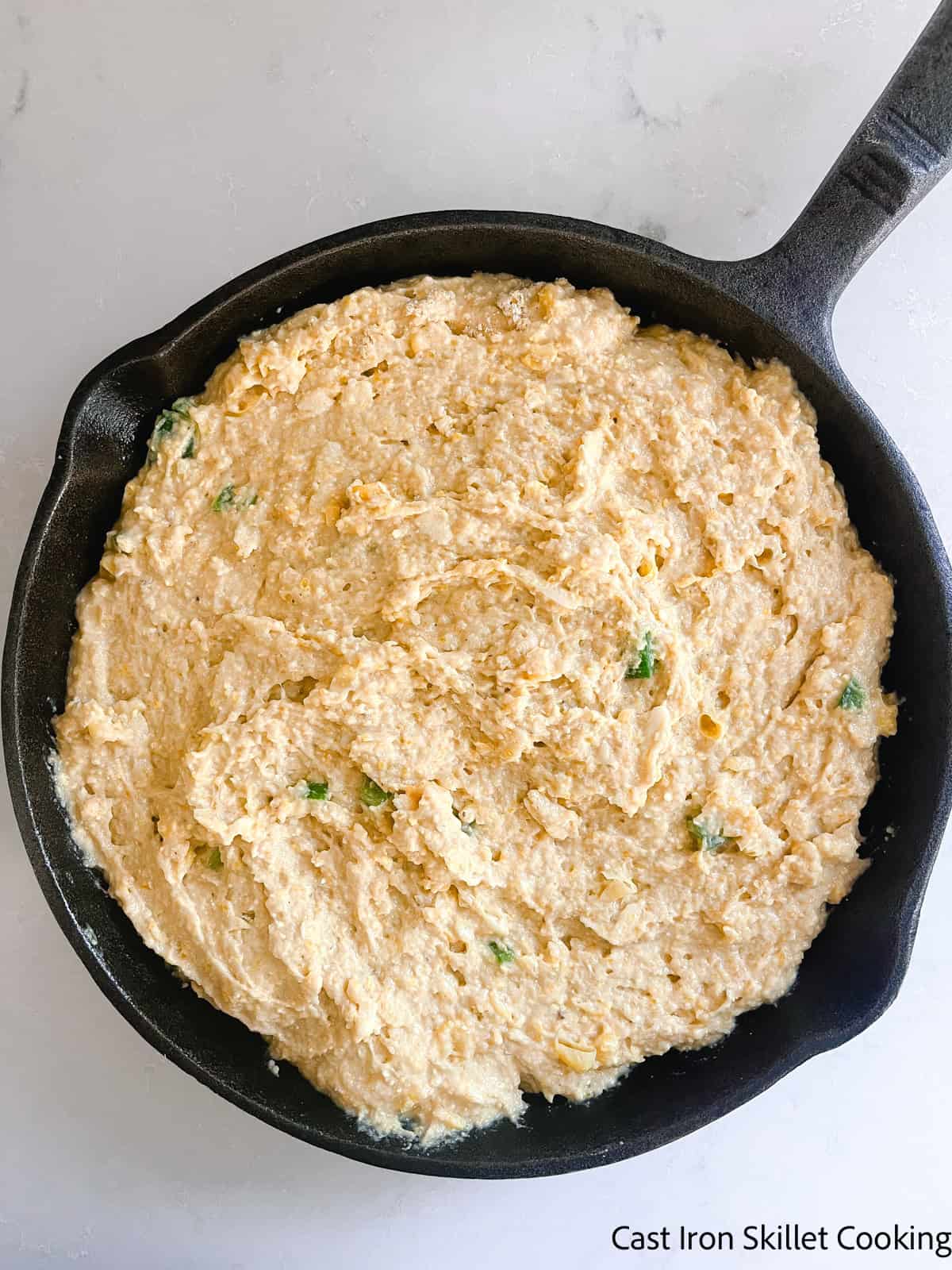 Fresh milled cornbread batter spread in a cast iron skillet before baking.