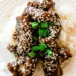 Garlic ginger venison on a bed of white rice with sesame seeds and green onions on top.
