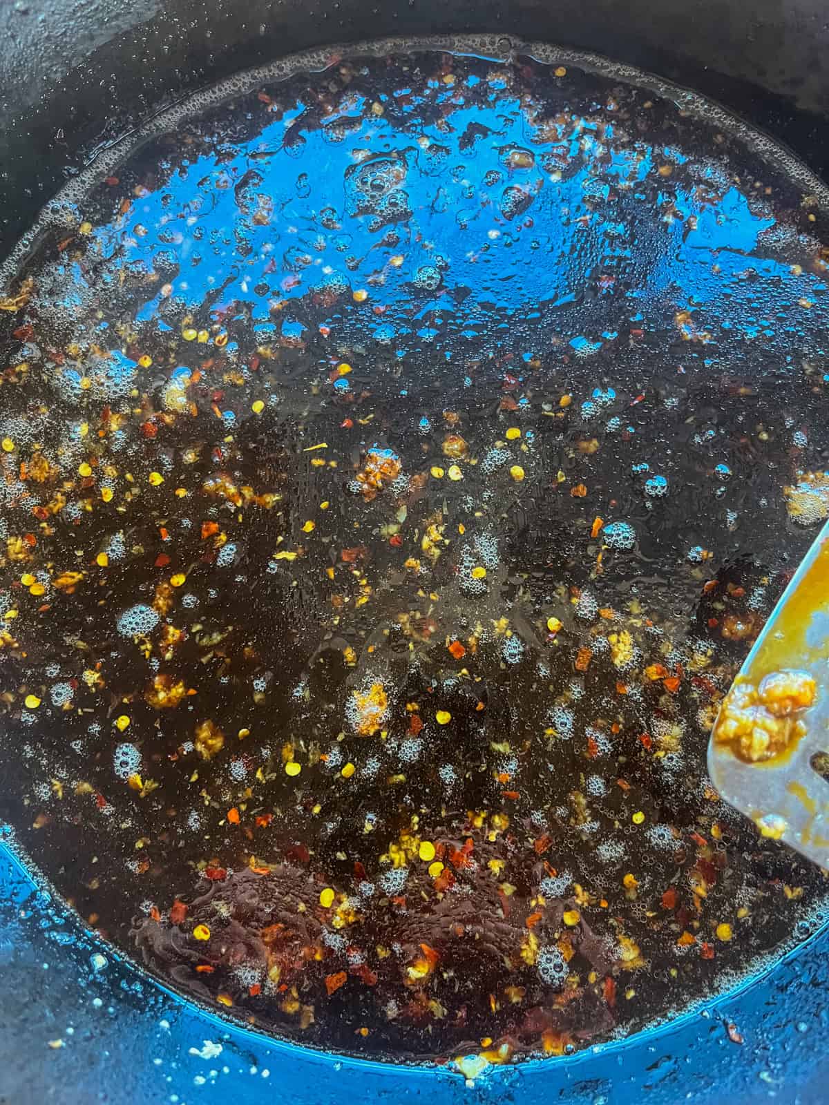 Adding liquids to the cast iron skillet with the ginger and garlic and scraping with a spatula.