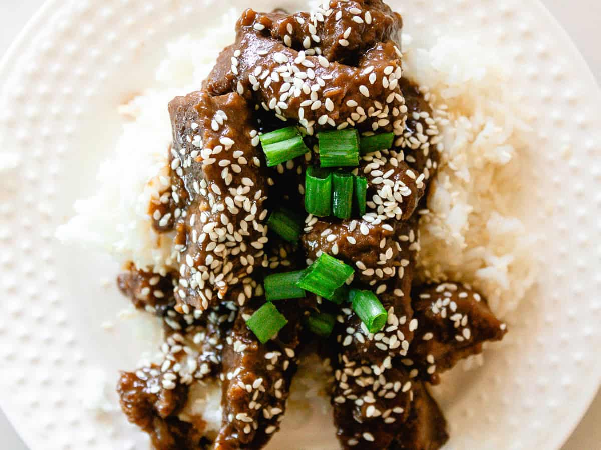 Garlic ginger venison on a bed of white rice with sesame seeds and green onions on top.