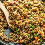 A cast iron skillet filled with venison fried rice with a wooden serving spoon.