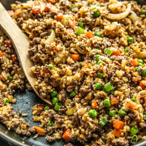 A cast iron skillet filled with venison fried rice with a wooden serving spoon.