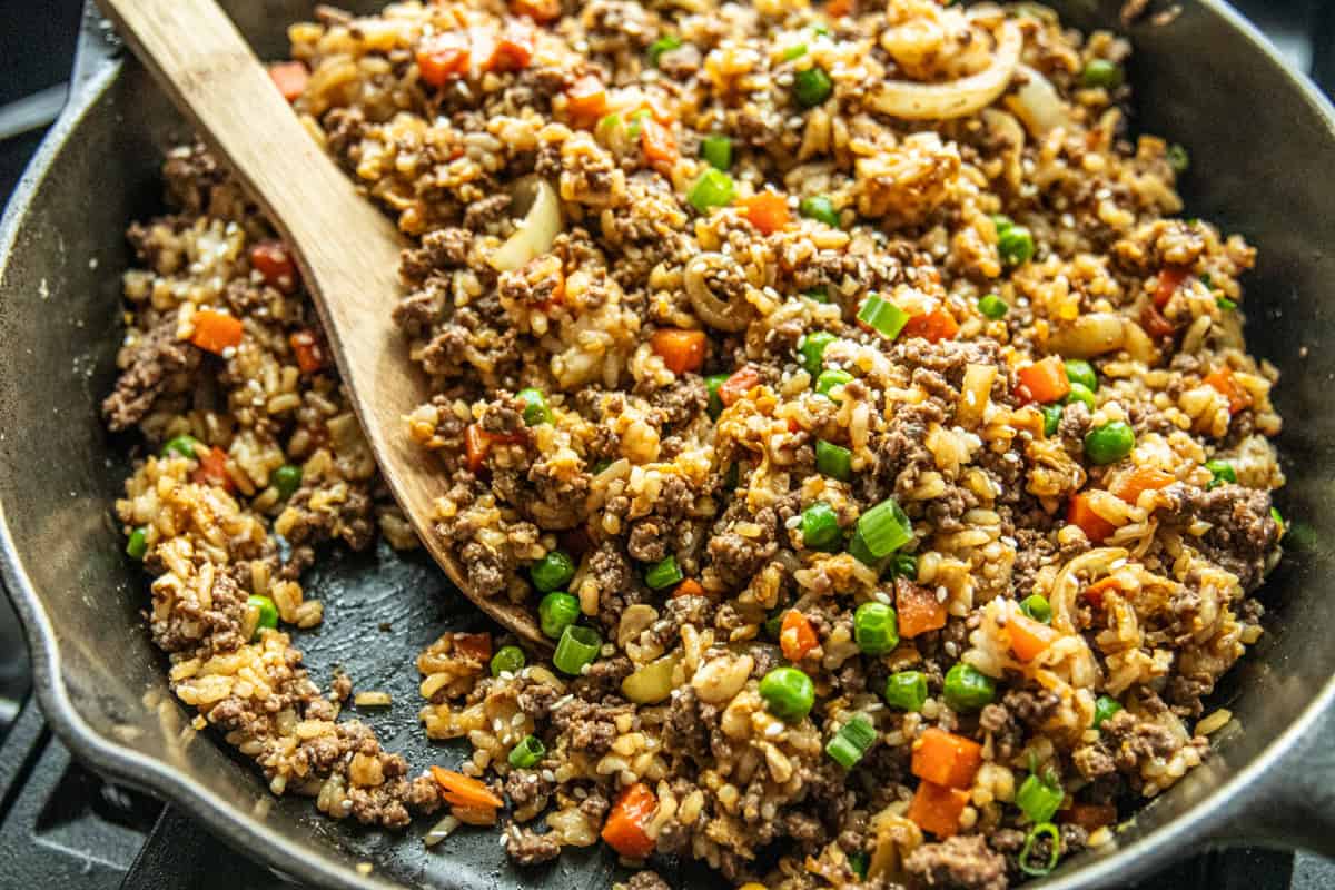 A cast iron skillet filled with venison fried rice with a wooden serving spoon.