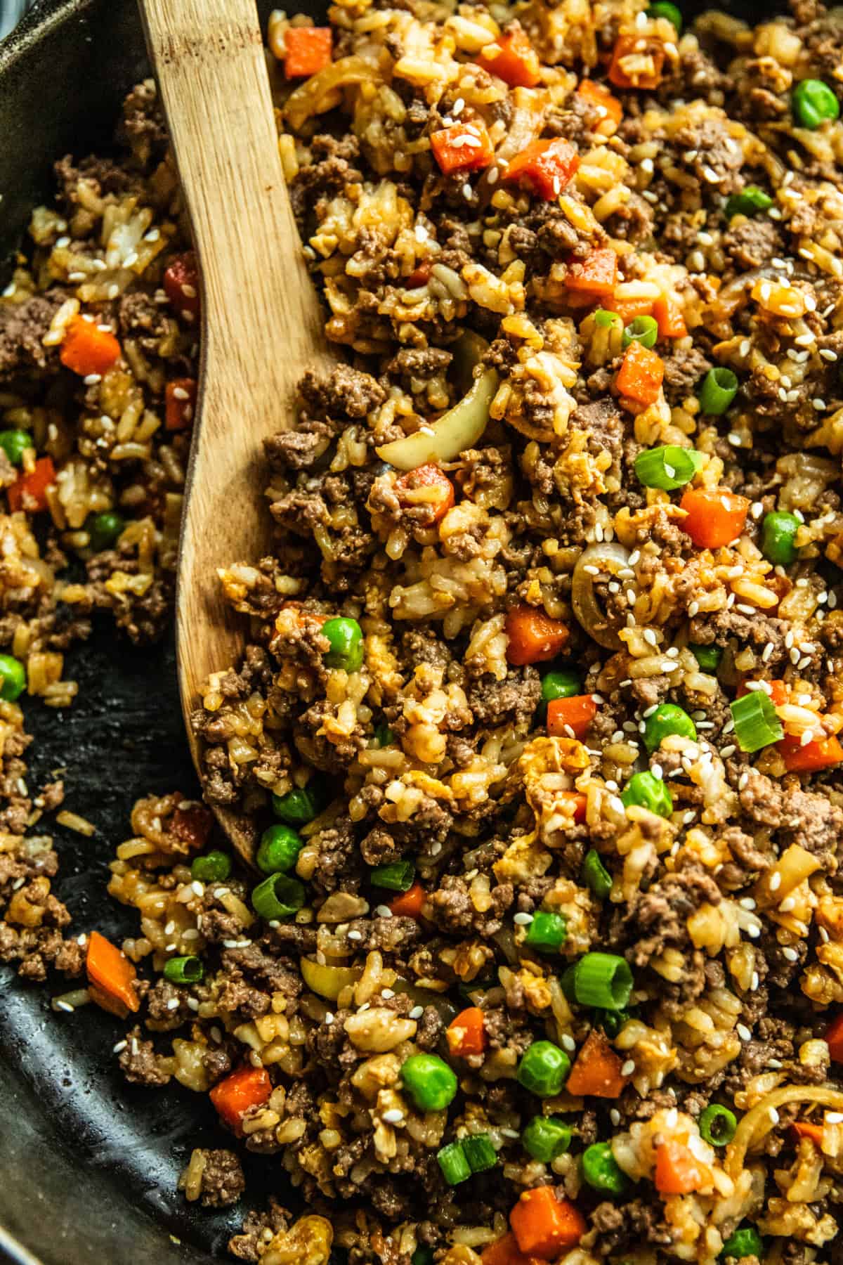 Venison fried rice in a cast iron skillet with a wooden serving spoon.