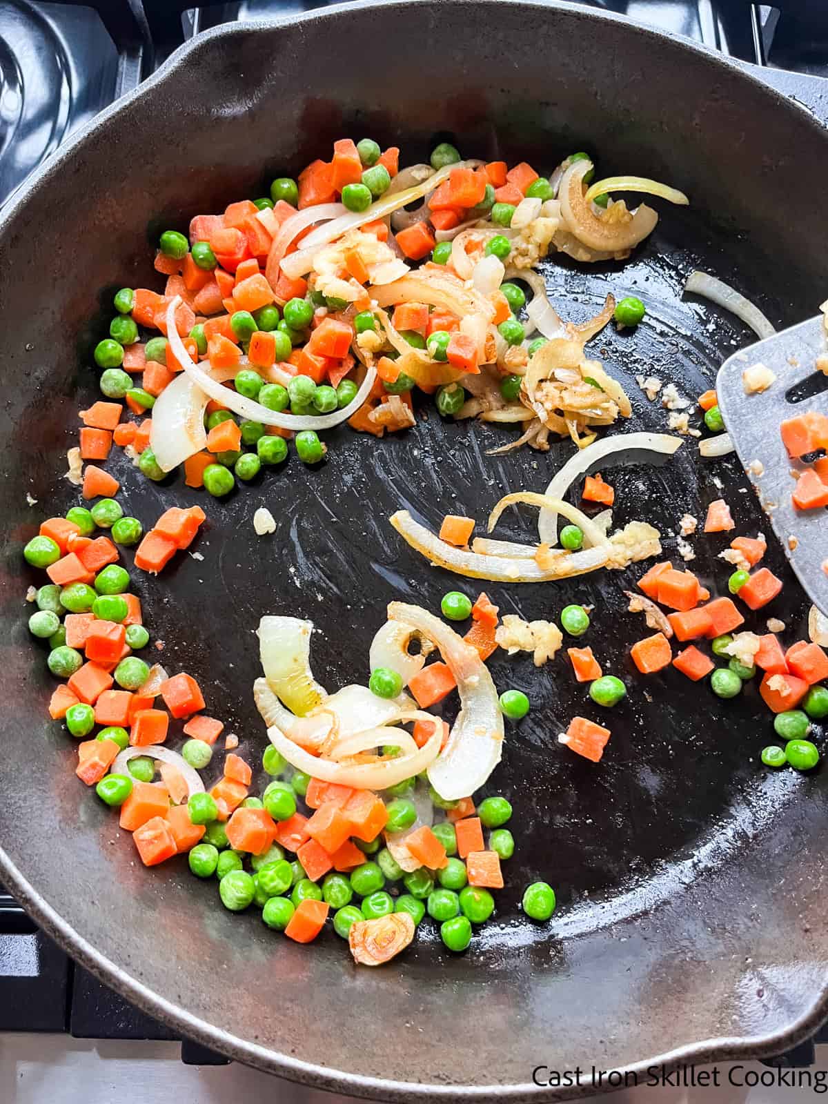 Sauteing carrots, peas, and onions in a cast iron skillet.