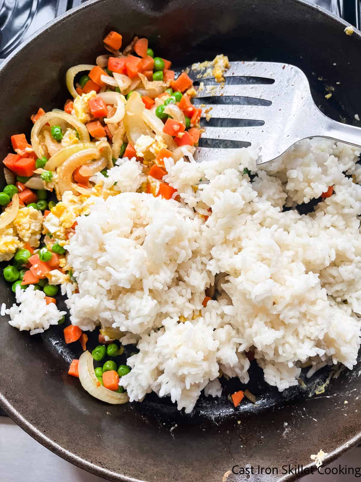 Adding cold cooked rice to the cast iron skillet with veggies and eggs.