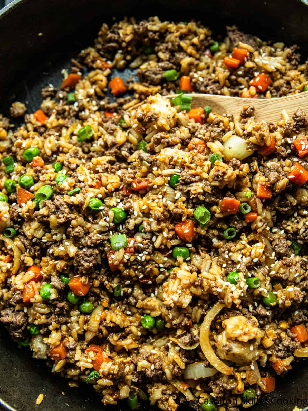 Venison fried rice in a cast iron skillet with a wooden spoon.