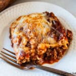 A slice of venison lasagna on a white plate with a fork.