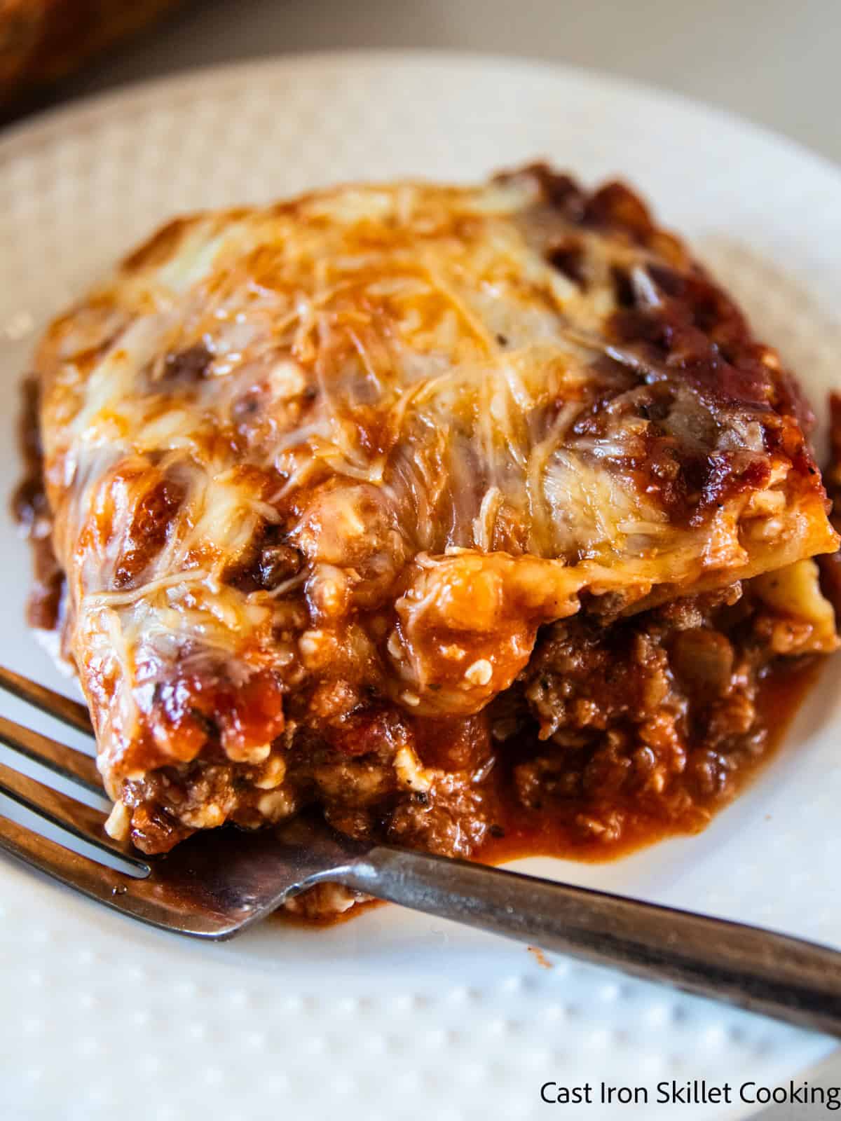 A slice of venison lasagna on a white plate with a fork.