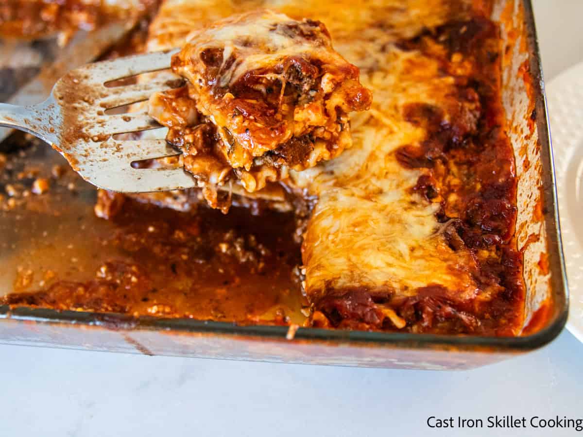 Scooping a slice of venison lasagna out of a baking dish.