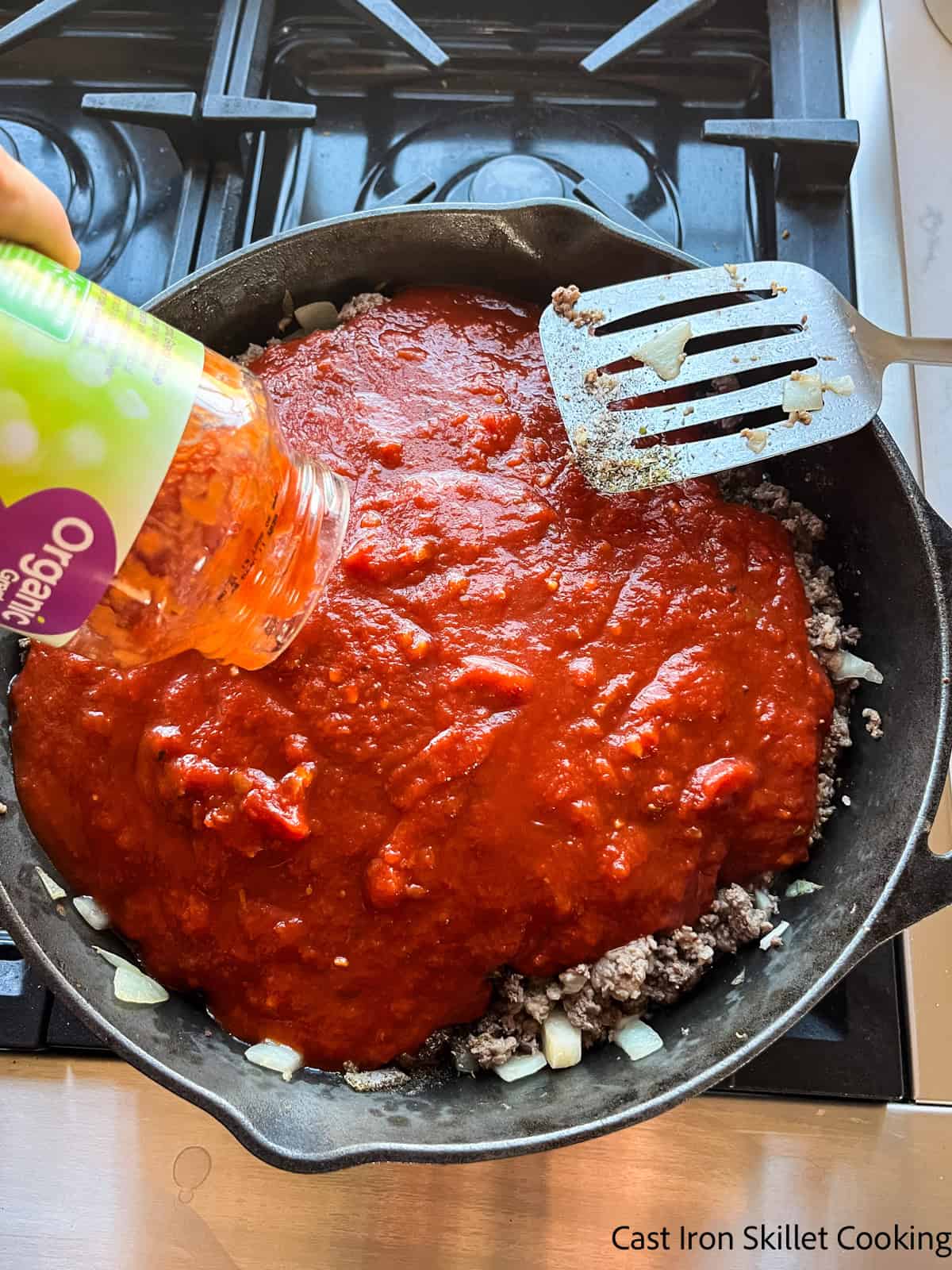 Pouring pasta sauce into a skillet with meat and onions.