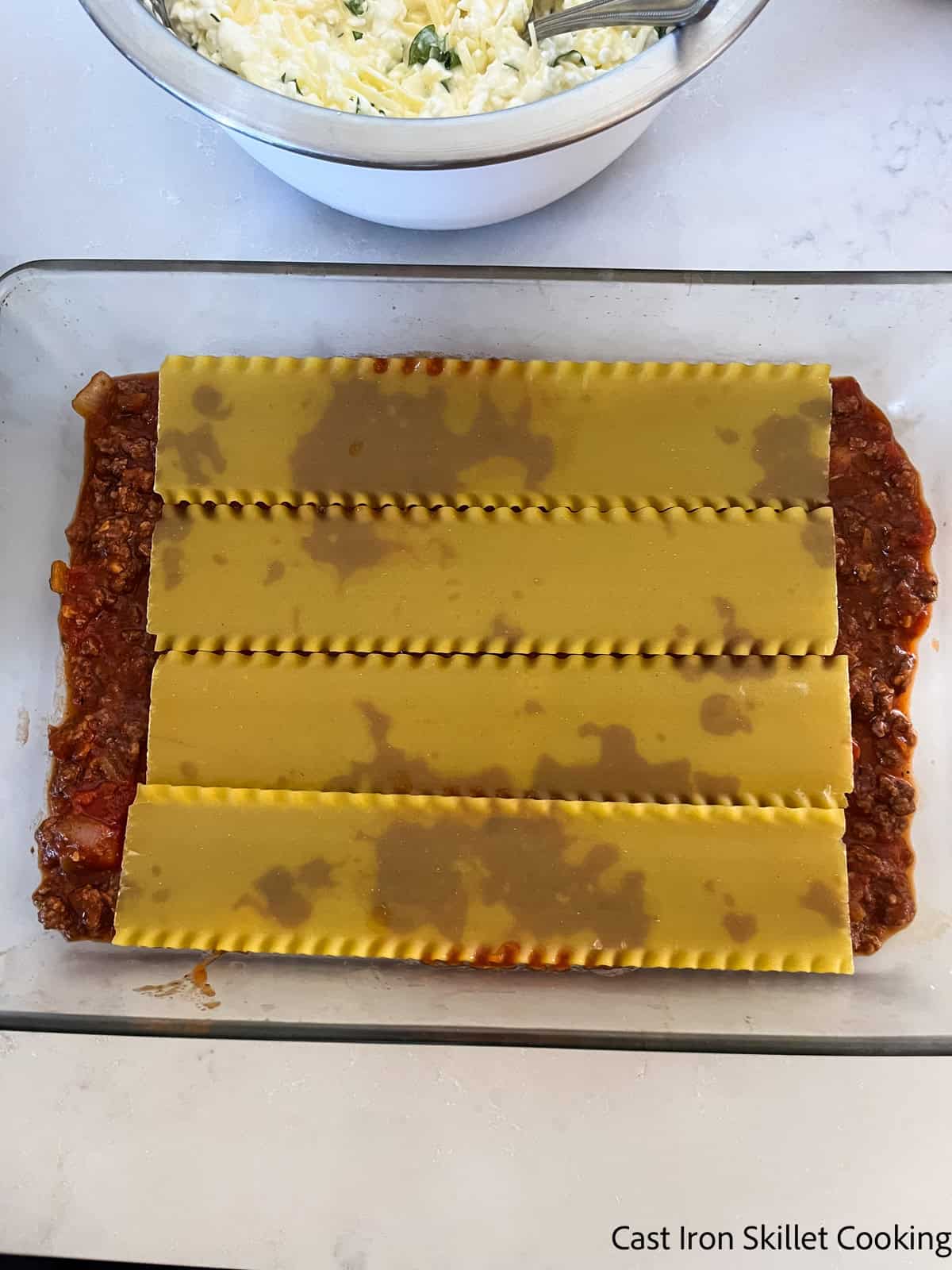 A baking dish with pasta sauce and lasagna noodles layered in the bottom.