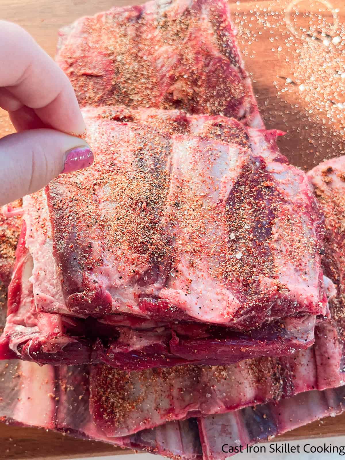 Sprinkling seasoning over uncooked venison ribs.