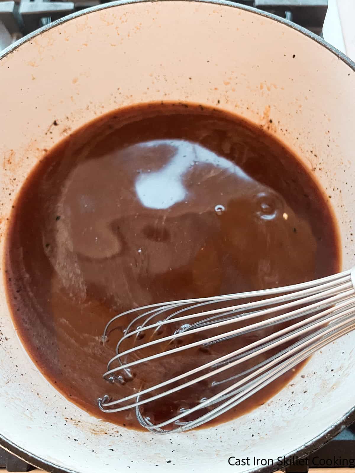 Stirring BBQ sauce and broth mixture in a bowl with a whisk.