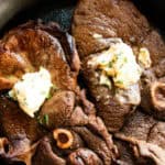 Garlic butter venison sirloin steaks in a cast iron skillet.