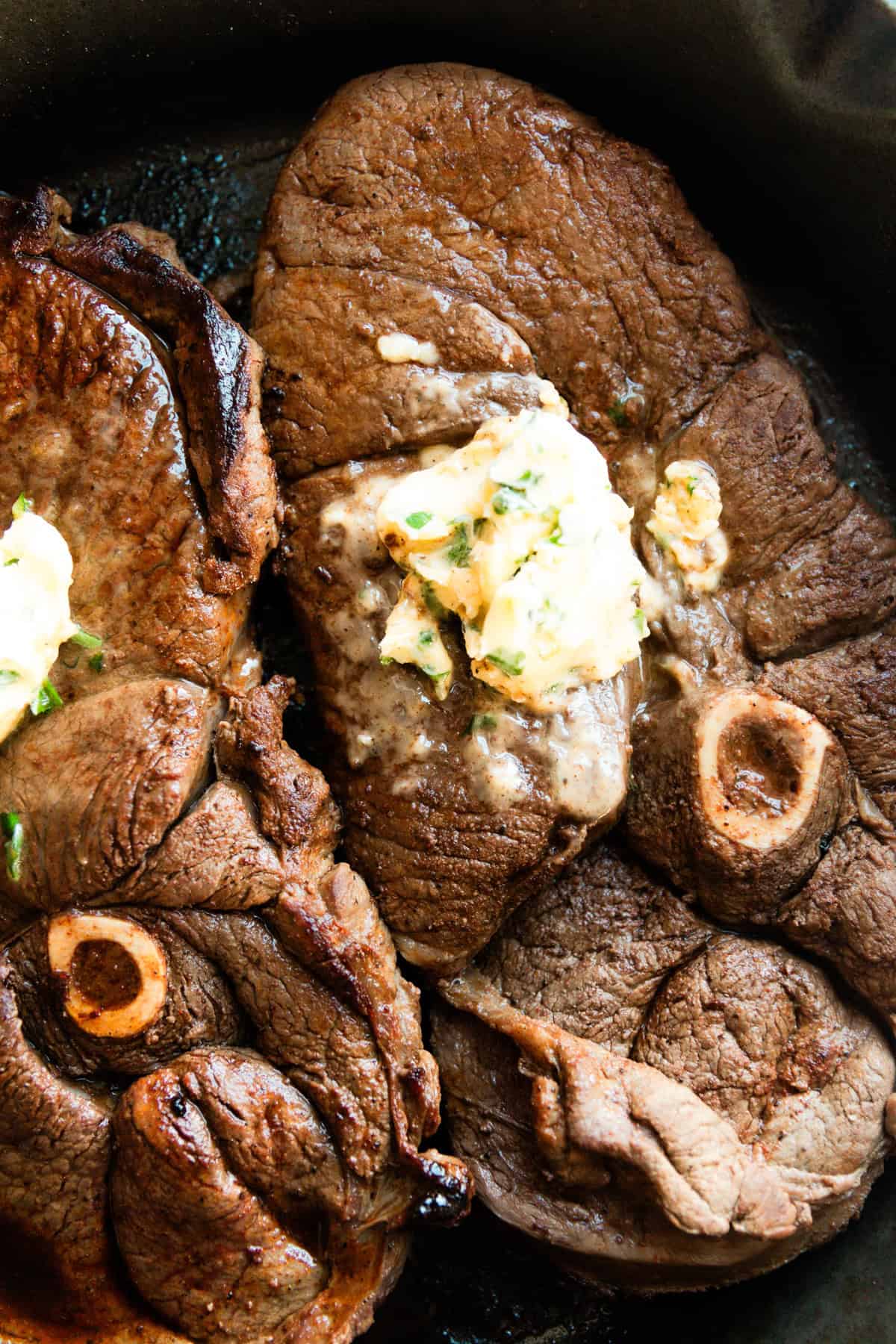 Two venison sirloin steaks in a cast iron skillet with a large dollop of garlic butter on top of each.