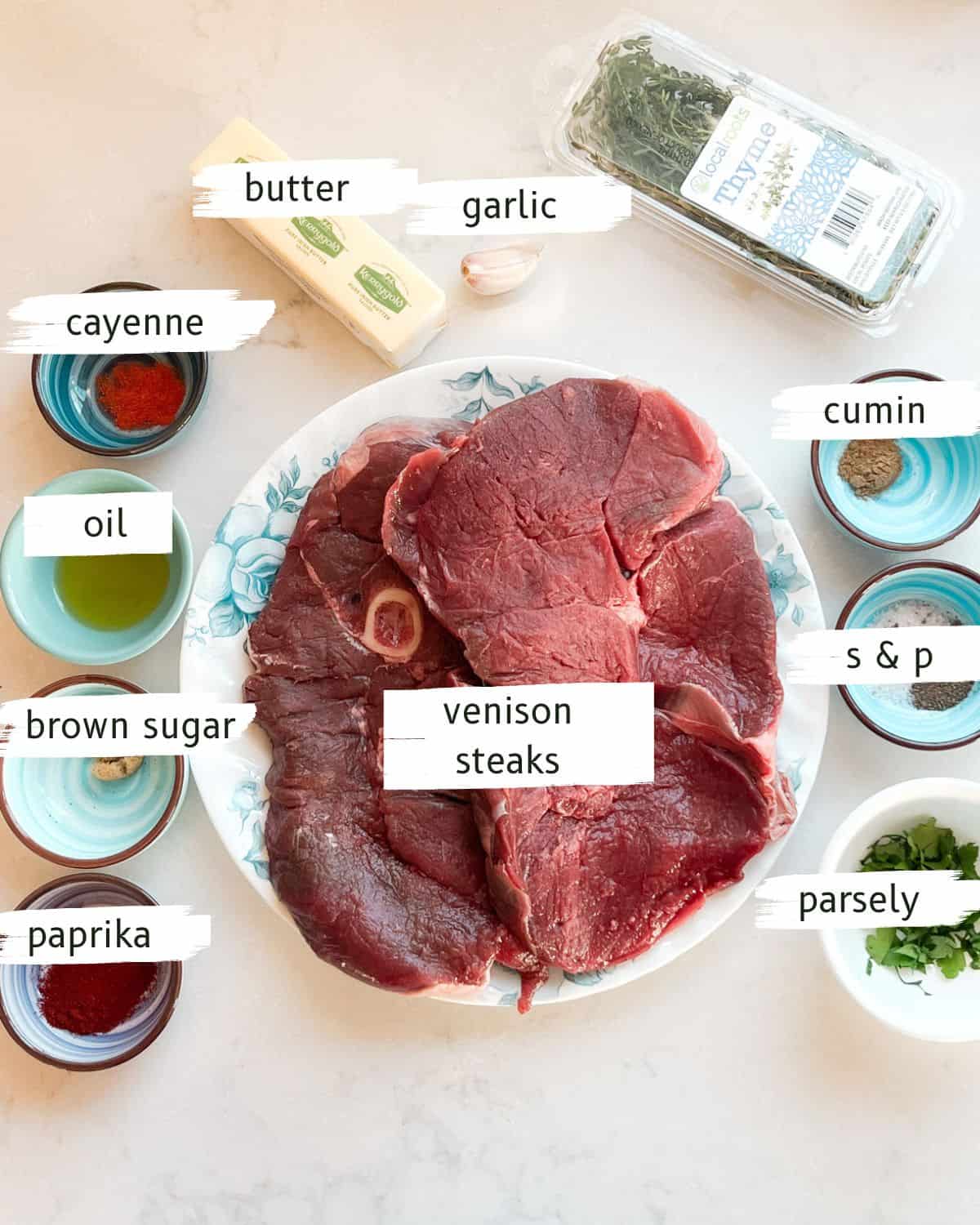 Venison sirloin steaks and garlic butter ingredients labeled on a white table.