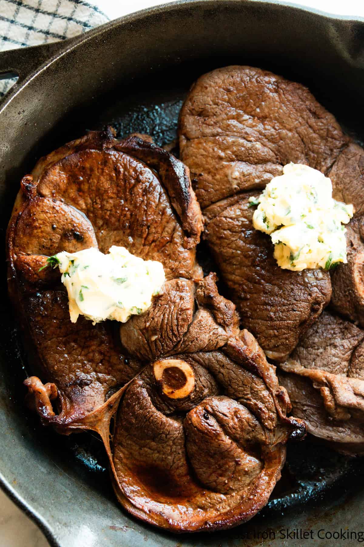 Venison sirloin steaks in a cast iron skillet topped with garlic butter.