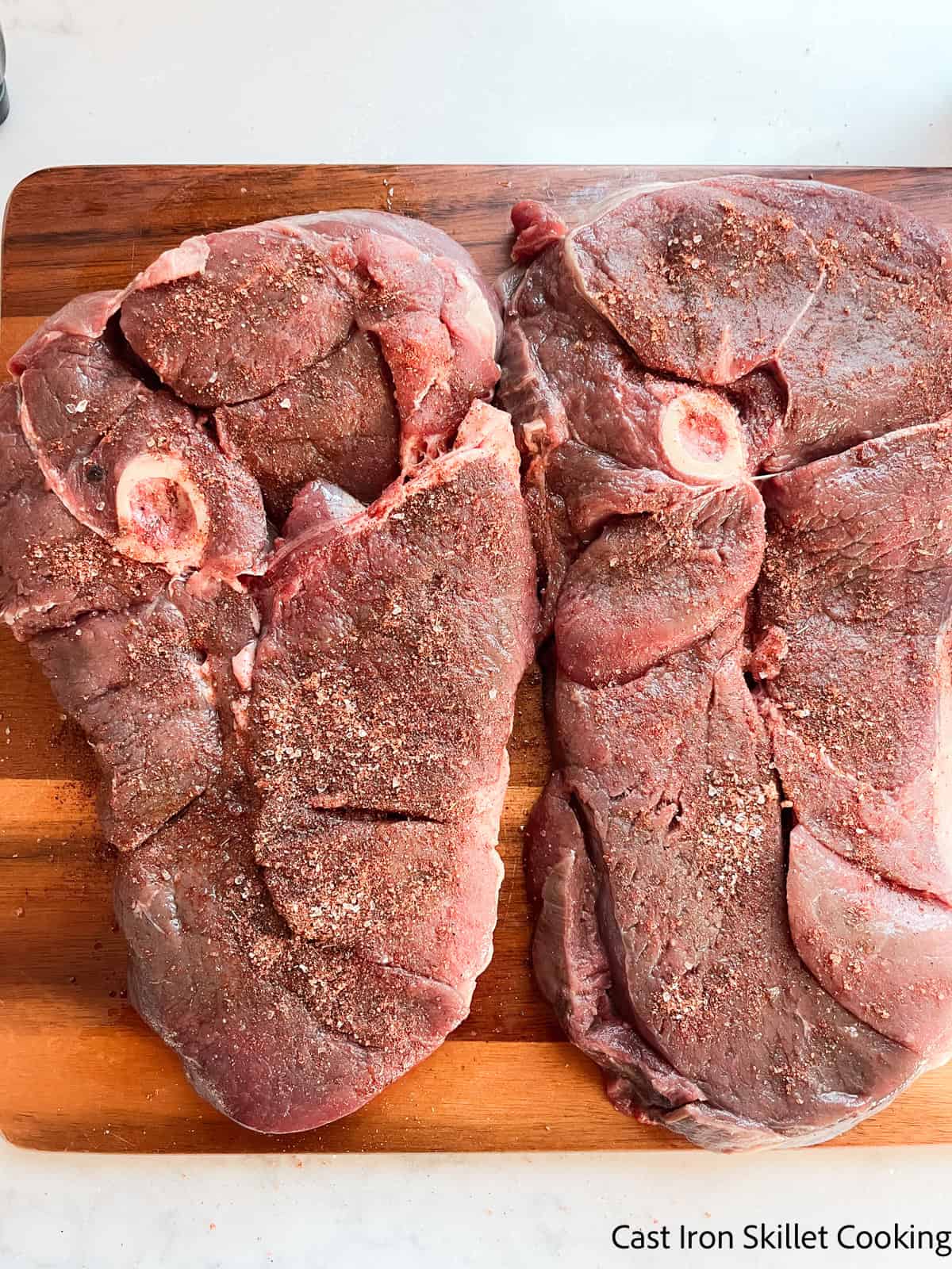 Venison sirloin steaks uncooked on a wooden board with seasoning rubbed in.