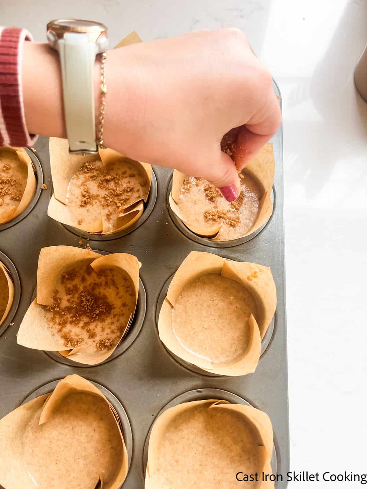 Sprinkling cinnamon sugar topping on unbaked muffins.