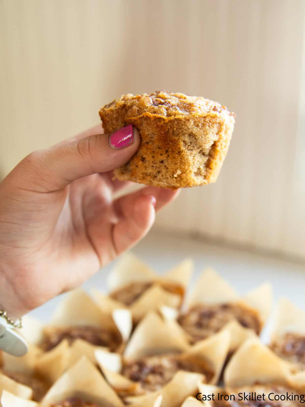 Holding up a whole grain cinnamon sugar muffin with more muffins in the background.