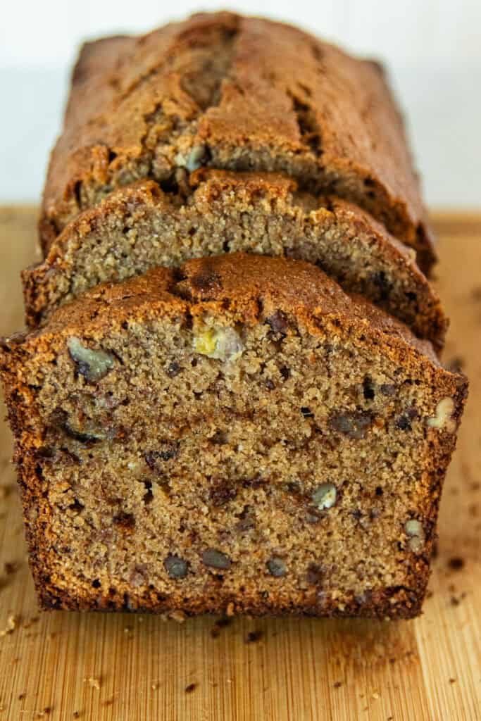 A sliced loaf of fresh milled banana bread on a wooden cutting board.