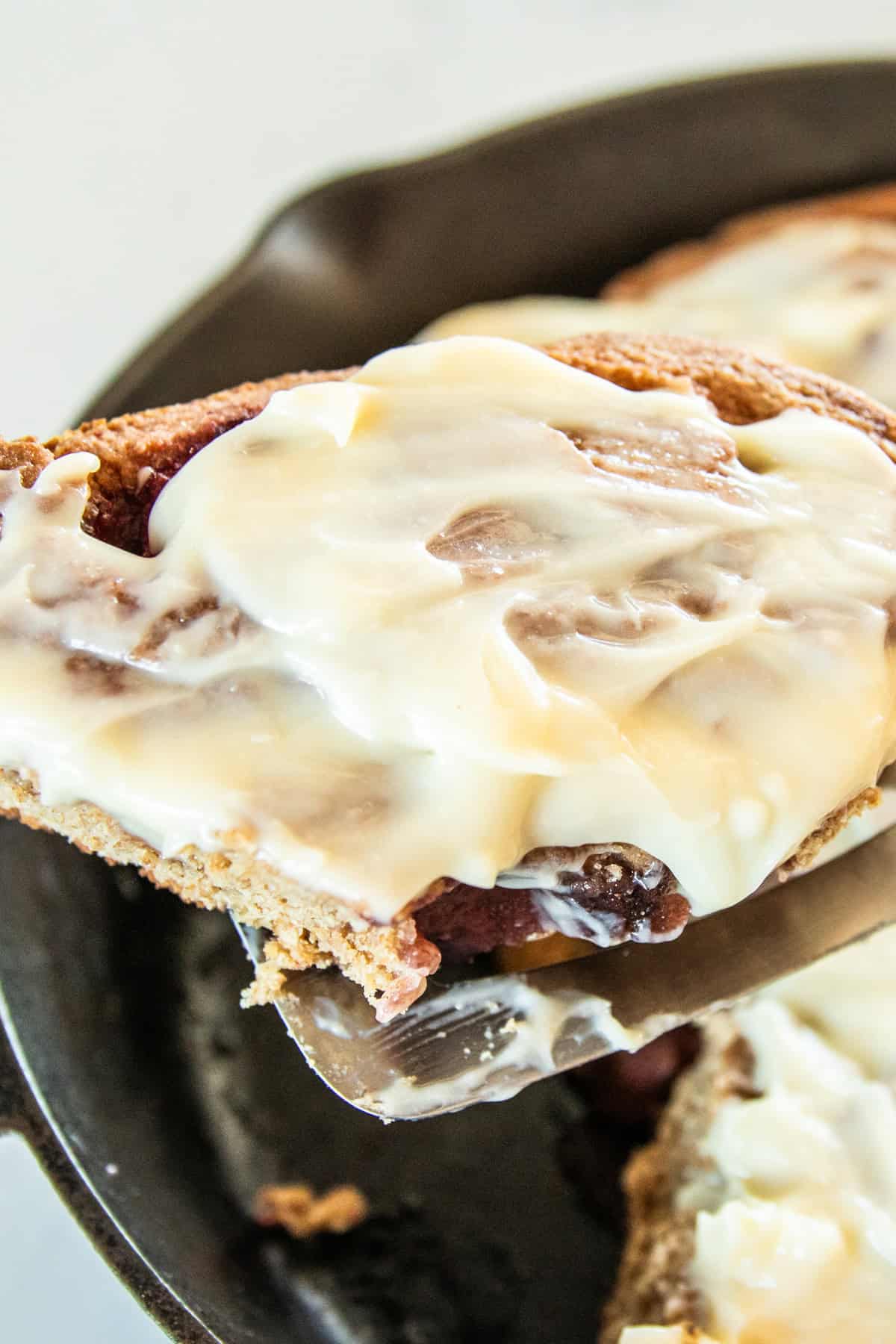 A close-up of a strawberry sweet roll being held over a cast iron pan of rolls.
