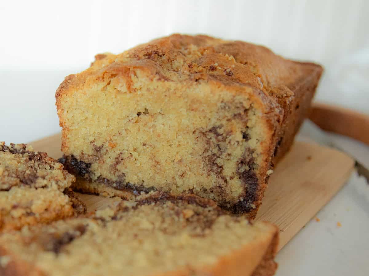 Freshly milled cinnamon swirl bread on a wooden cutting board with thick slices next to it and deep cinnamon crumble exposed!
